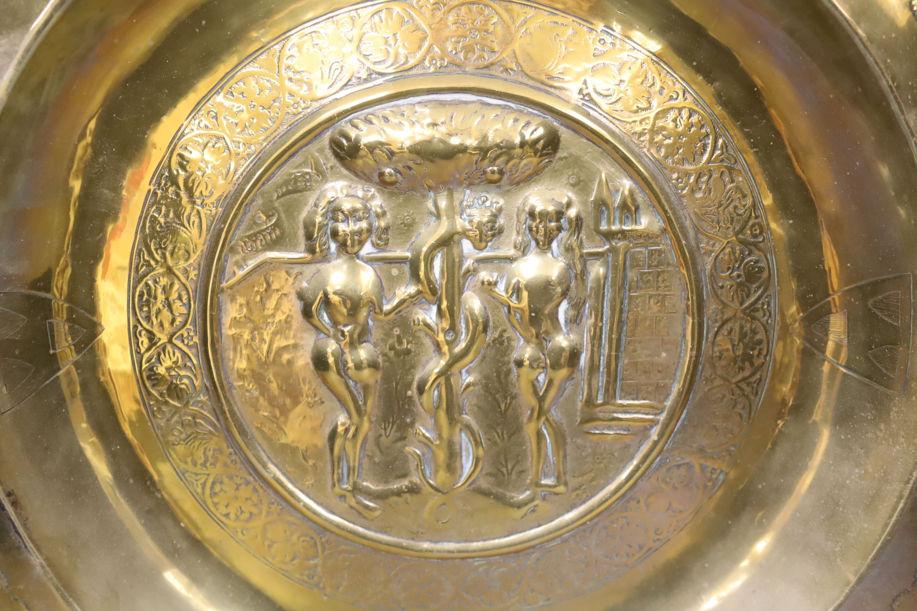 A large Nuremberg brass alms dish, 17th century, depicting Adam and Eve within a twisted foliate and floral border, with stylised armorial shields, 42cm